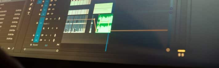 Capture rapprochée d’un écran d’ordinateur affichant une timeline de montage vidéo avec des pistes audio, des effets et des transitions dans un logiciel professionnel.