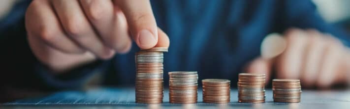 Main empilant des pièces de monnaie par petites colonnes, symbolisant un budget limité pour créer du contenu vidéo de qualité.